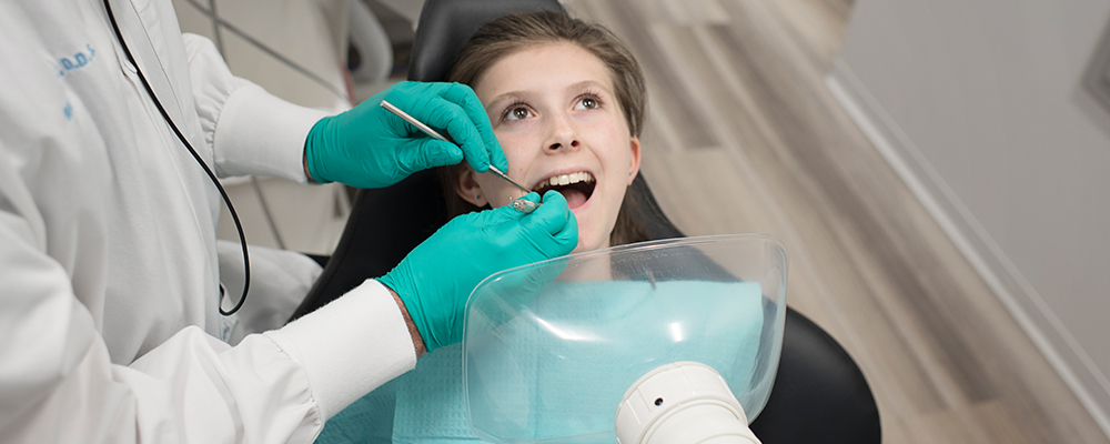 Picture of a young woman seated in dental chair with aerosol vacuum near her face.