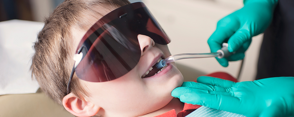 Picture of a young boy wearing dark eye shields with a suction tube in his mouth.