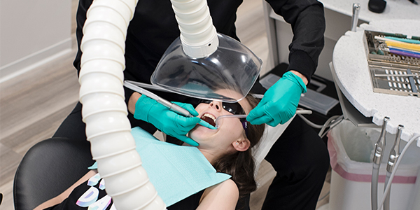Young girl in dentist's chair with large aerosol suction device near her face.