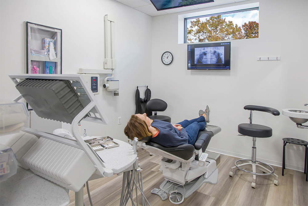 Woman with brown hair reclined in dental chair with x-ray image of a mouth on the wall.